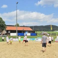 oberbauerschaft-sportplatz-festplatz-02.jpg Gruppe von Menschen spielt Beachvolleyball auf einem Sandplatz mit grüner Landschaft und Gebäuden im Hintergrund.