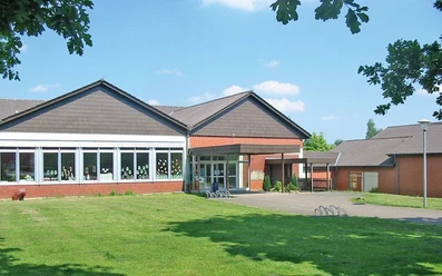 oberbauerschaft-ev-grundschule-oberbauerschaft-01.jpg Das Bild präsentiert ein rotes Backsteingebäude mit großzügigen Fenstern und einer Grünfläche davor.