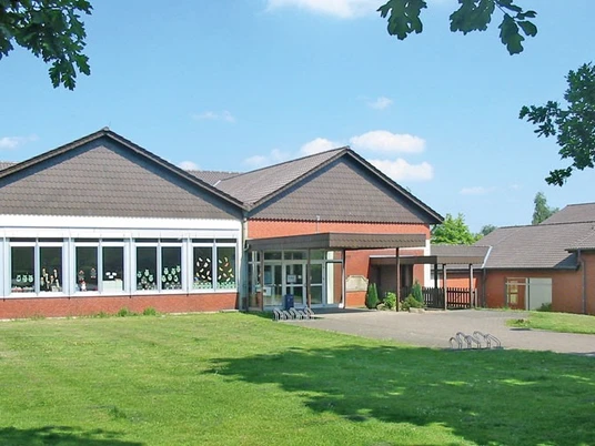 oberbauerschaft-ev-grundschule-oberbauerschaft-01.jpg Das Bild präsentiert ein rotes Backsteingebäude mit großzügigen Fenstern und einer Grünfläche davor.