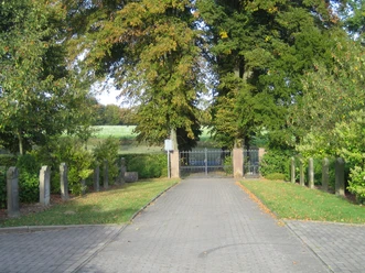 oberbauerschaft-friedhof-beendorf.JPG Eingang zu einem ländlichen Friedhof mit Tor und Bäumen, gesäumt von alten Grabsteinen.