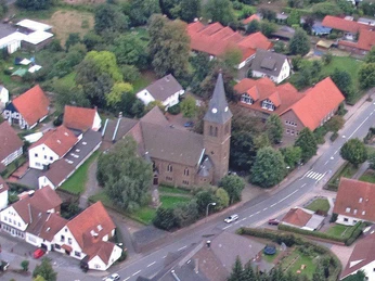 Kirche Schnathorst Luftaufnahme einer Kirche in einem Dorf mit rotdächigen Häusern und grünen Bäumen umgeben.