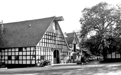schnathorst-hof-niedermeier-01.jpg Historischer Fachwerkhof mit großen Scheunen und hohen Giebeldächern, umgeben von Bäumen.