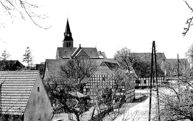 schnathorst-hof-niedermeier-03.jpg Fachwerkhäuser in einer Dorfansicht mit einer Kirche im Hintergrund, winterliche Baumkronen säumen die Straße.