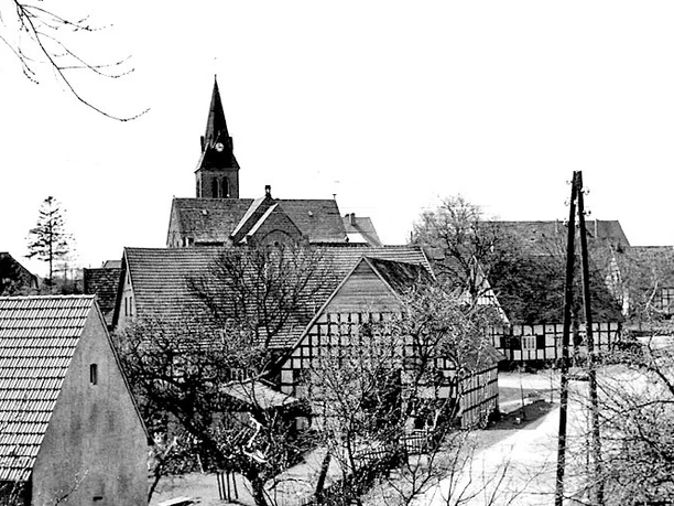 schnathorst-hof-niedermeier-03.jpg Fachwerkhäuser in einer Dorfansicht mit einer Kirche im Hintergrund, winterliche Baumkronen säumen die Straße.