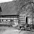 schnathorst-hof-wegener.jpg Schwarz-weißes historisches Fachwerkgebäude mit altem Holzkarren vor Strohballen und Bäumen.