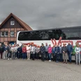 FStadtrundfahrtStadtführerVHS_.jpg Vor einem modernen Reisebus der Firma 'Witter' posiert eine gemischte Gruppe von etwa 24 Personen, darunter Männer und Frauen unterschiedlichen Alters. Der Hintergrund zeigt ein traditionelles Fachwerkhaus, während der Himmel grau und wolkenverhangen wirkt.