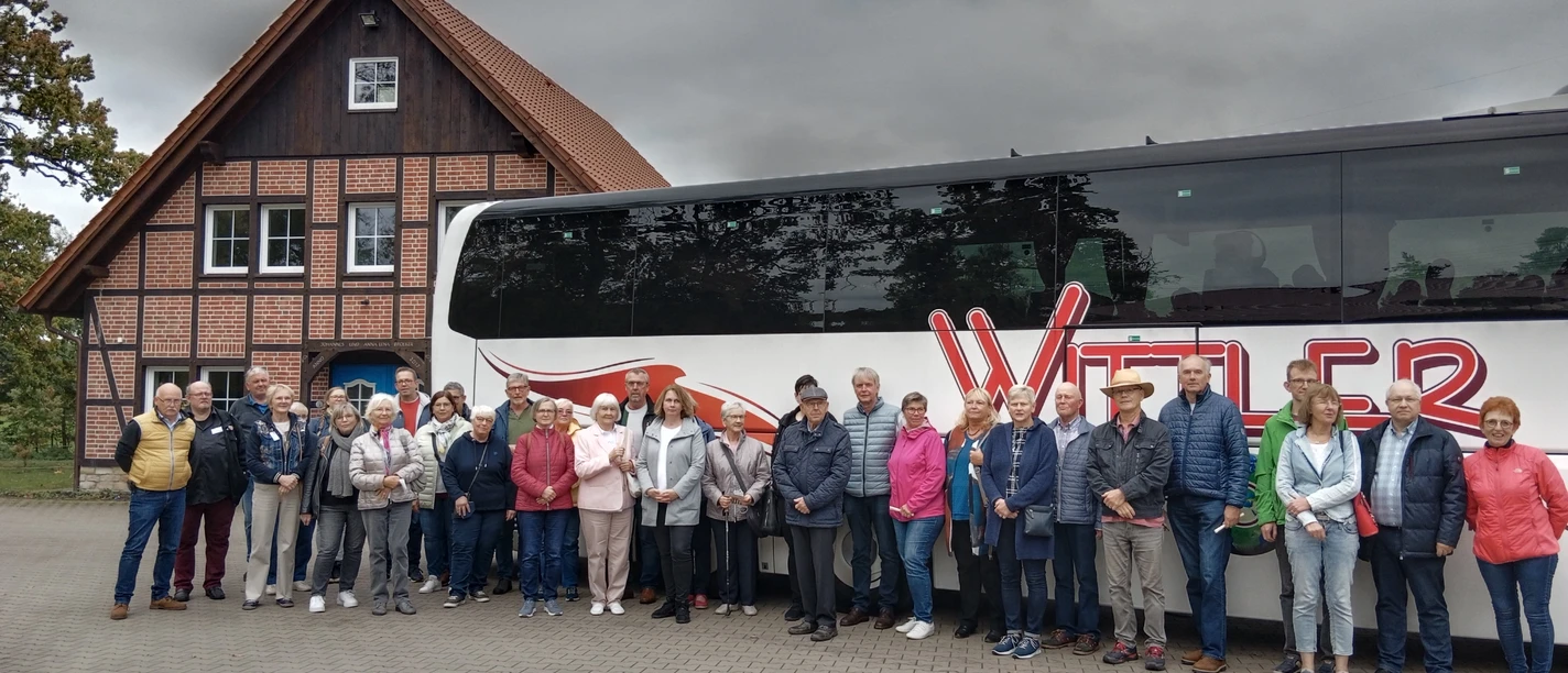 FStadtrundfahrtStadtführerVHS_.jpg Vor einem modernen Reisebus der Firma 'Witter' posiert eine gemischte Gruppe von etwa 24 Personen, darunter Männer und Frauen unterschiedlichen Alters. Der Hintergrund zeigt ein traditionelles Fachwerkhaus, während der Himmel grau und wolkenverhangen wirkt.