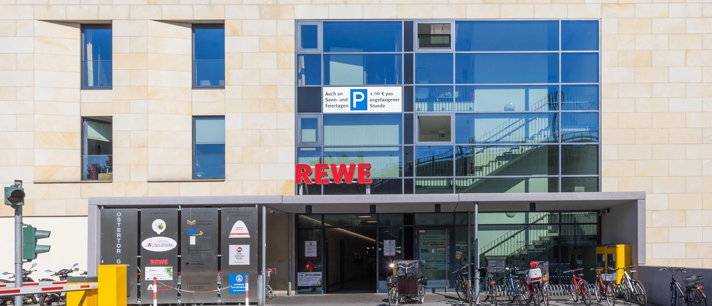 Eingang zum REWE-Markt in Bad Salzuflen mit Glasfassade, Fahrrädern und Parkschranke
