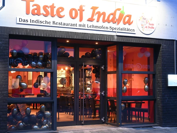 A Taste of India außen.JPG Taste of India Restaurantfront mit großen Glasfenstern, darunter schwarze und goldene Luftballons.