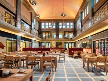 Restaurant KWB im Stadtpalais Hölzerne Tische und Stühle sind stilvoll in einem offenen, hellen und elegant aussehenden Raum mit hohen Decken arrangiert.Wooden tables and chairs are stylishly arranged in an open, bright and elegant-looking room with high ceilings.