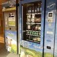 Milchautomat Bichlerhof, Farchant im kleinen Holzhäusl steht linkerhand ein Milchautomat mit Flaschen, rechts davon zwei Automaten mit Yogurt, Wurst und Fleischauswahl, vakumiert. in der Mitte findet sich der Bezahlautomat