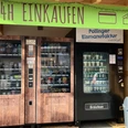 Lebensmittelautomat in FArchant 2-türiger Kühlschrank mit verschiedenen regionalen Lebensmitteln sowie ein Maschine für Softeis, darüber steht auf grünem Banner : 24 Stunden einkaufen zu bezahlen in bar und mit Karte
