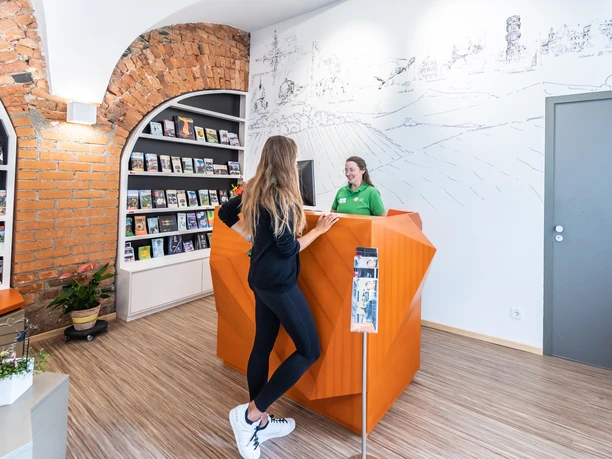 Two people at the visitor reception of a modern tourism center with information material.
