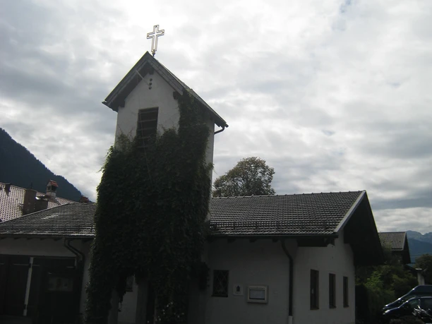 Aussenansicht der Kirche mit Kreuz und mit von Efeu umranktem Turm