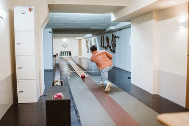 Kegeln im Brauhaus Koelsche Boor (13).jpg Eine Person in Jeans und orangefarbener Jacke spielt Kegeln in einem Innenraum mit Holzboden.</p>