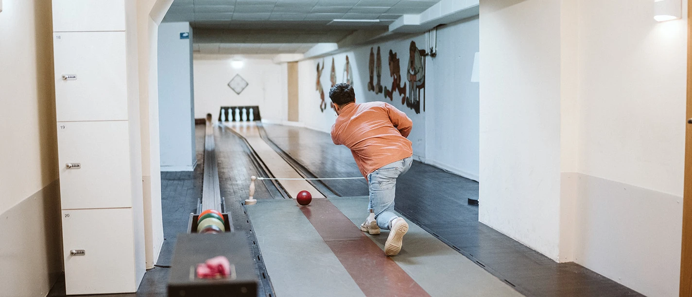 Kegeln im Brauhaus Koelsche Boor (13).jpg A person in jeans and an orange jacket plays skittles in an indoor room with a wooden floor.</p> <p