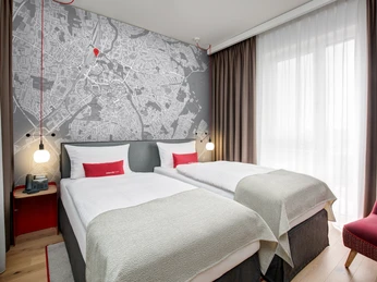 ICH_Herford_Zimmer_Montage_high.jpg Hotelzimmer mit zwei Einzelbetten, großer Raumkarte als Wandbild, modernem Dekor und Tageslicht.