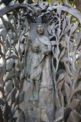 Bronzene Stele mit filigranem Blattwerk und Figuren, dargestellt als Frau mit Kind in sanfter Pose.