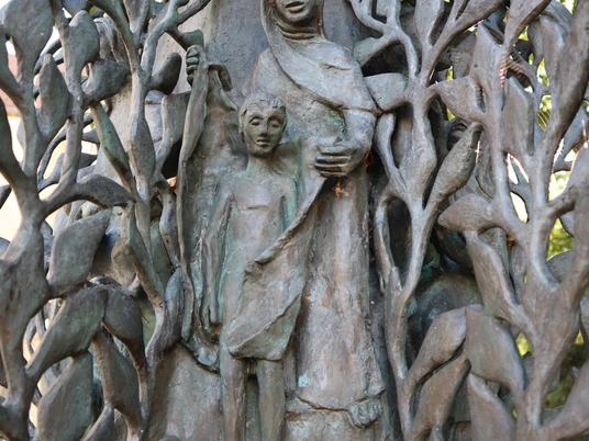 Bronzene Stele mit filigranem Blattwerk und Figuren, dargestellt als Frau mit Kind in sanfter Pose.
