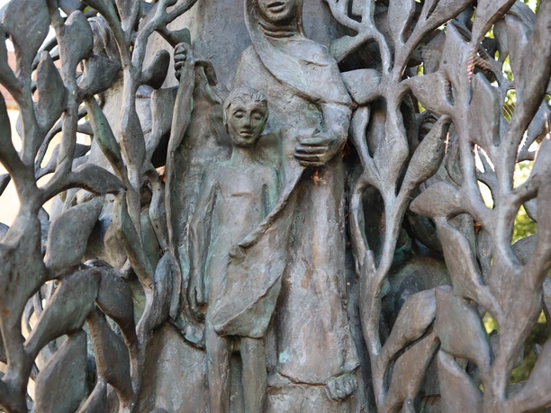 Abtei-Stele (6).JPG Bronzene Stele mit filigranem Blattwerk und Figuren, dargestellt als Frau mit Kind in sanfter Pose.