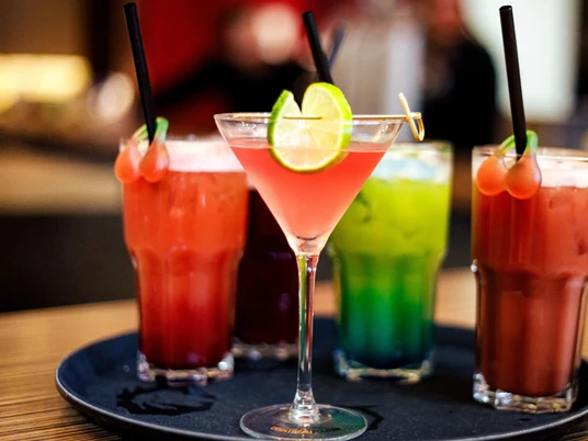 Eine Auswahl an bunten Cocktails, darunter ein rosa Martini mit Limettenscheiben auf einem Tablett.