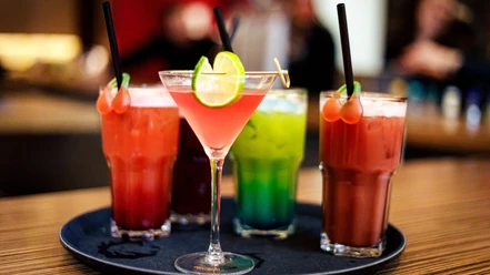 Cocktails Weekend Cocktailbar Eine Auswahl an bunten Cocktails, darunter ein rosa Martini mit Limettenscheiben auf einem Tablett.