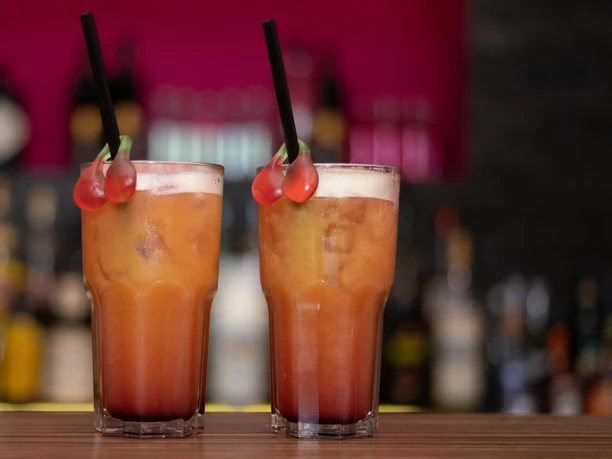 Zwei bunte Cocktails mit Kirschen als Dekoration stehen auf einem Tresen vor einer unscharfen Bar.