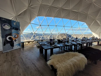 Island Landschaft Innenraum eines geodätischen Kuppelzeltes mit gedeckten Tischen und Bergblick durch große Fenster.Interior of a geodesic dome tent with covered tables and mountain views through large windows.