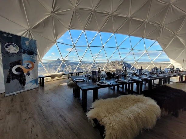 Island Landschaft Interior of a geodesic dome tent with covered tables and mountain views through large windows.