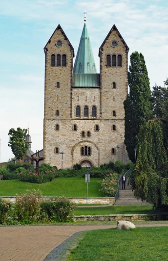 Abdinghofkirche in Paderborn vor blauem Himmel, umgeben von grünen Rasenflächen und Bäumen.
