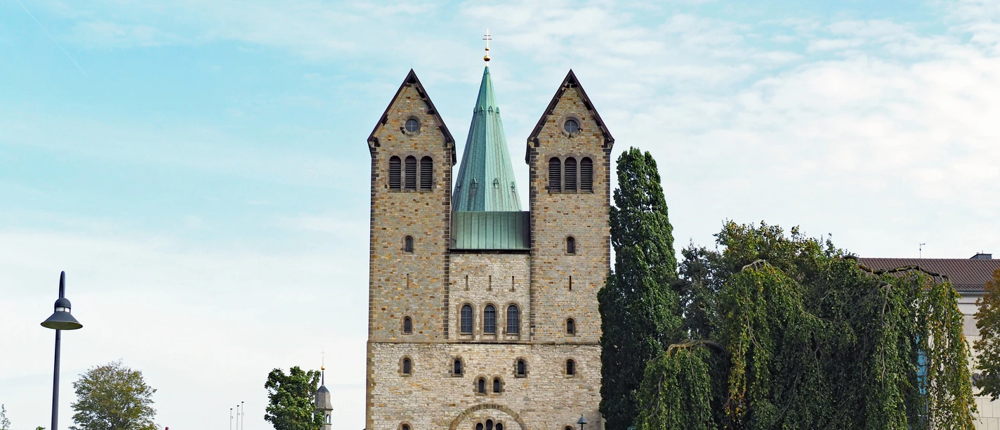Abdinghofkirche Abdinghofkirche in Paderborn vor blauem Himmel, umgeben von grünen Rasenflächen und Bäumen.