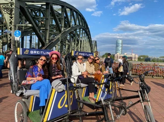 Rikolonia Champagnerfahrt.jpg Fünf Frauen sitzen in einer Fahrrad-Rikscha vor einer Brücke mit Vorhängeschlössern und genießen den Ausblick.</p>