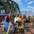 Rikolonia Champagnerfahrt.jpg Fünf Frauen sitzen in einer Fahrrad-Rikscha vor einer Brücke mit Vorhängeschlössern und genießen den Ausblick.</p>Five women sit in a bicycle rickshaw in front of a padlocked bridge and enjoy the view.</p> <p