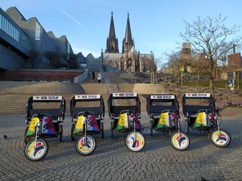 Rikolonia_Event Branding.jpg Die farbenfrohen Fahrradrikschas stehen vor dem eindrucksvollen Kölner Dom in der Abenddämmerung.The colorful bicycle rickshaws stand in front of the impressive Cologne Cathedral at dusk.