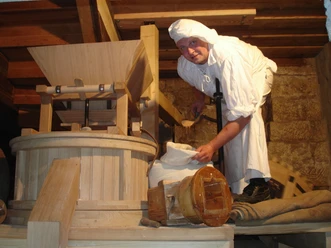 Bäcker beim Mehl mahlen in der Schmilk'schen Mühle Ein Bäcker in traditioneller Kleidung mahlt Mehl in einer historischen Holzmechanik in der Mühle.