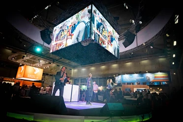 Frauenthal-Expo-Wien-PLUS-Messeband-Entertainment-DJplus-04.jpg Musiker auf einer Messebühne, große Bildschirme zeigen lebhafte Szenen, umgeben von Publikum.</p>