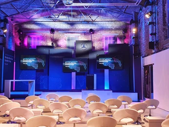 Halle_Produkteinführung Innenraum eines modernen Veranstaltungsraums mit lila Beleuchtung und weißen Sesseln.Interior of a modern event room with purple lighting and white armchairs.