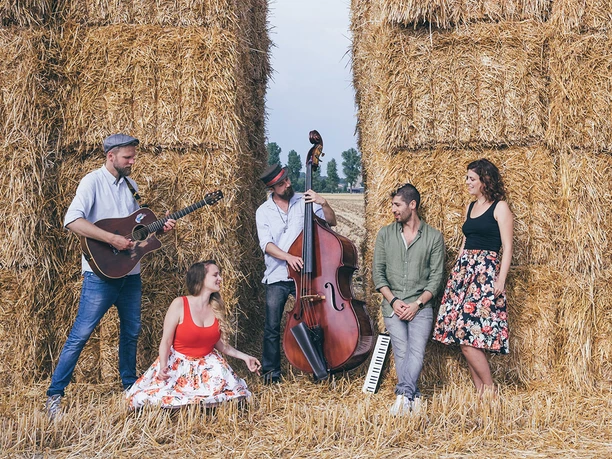 reinakustisch-akustikband-event-party-14.jpg Musicians play in front of stacked hay bales, with guitar, double bass and an accordion.
