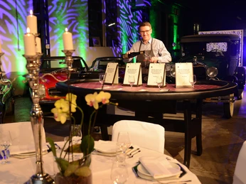Casino Vinophil. Genuss-Quiz Tisch Klassische Autos umgeben eine stilvoll gestaltete Gala mit Kerzenständern und gedeckten Tischen.Classic cars surround a stylishly designed gala with candlesticks and laid tables.