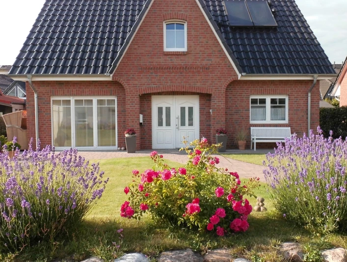 Titelbild Ein Backsteinhaus mit Solarpanelen, umgeben von Lavendel und Rosen in einem gepflegten Garten.