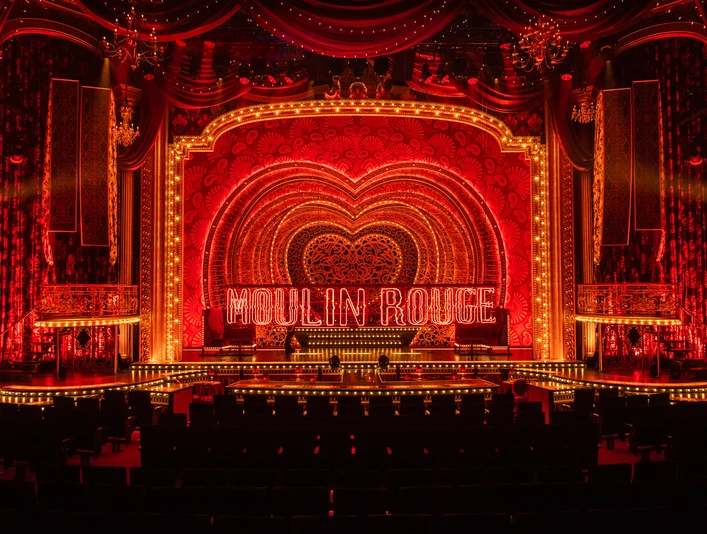 02_MDK_Saal_1 Beleuchtete Bühne des Moulin Rouge in Paris mit leuchtendem roten Herz und Schriftzug.</p>Illuminated stage of the Moulin Rouge in Paris with glowing red heart and lettering.</p> <p