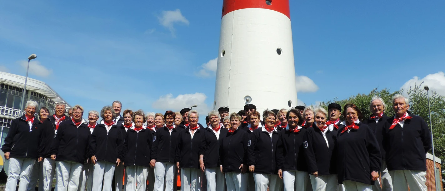 Nordseechor in Büsum Eine Gruppe Menschen in weißen Hosen und blauen Oberteilen. Im Hintergrund ein Leuchtturm.