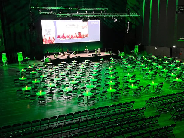 Consilium_live_23_002.jpg Ein großer Veranstaltungsraum mit vielen Stühlen und Tischen, in grünem Licht beleuchtet.</p>