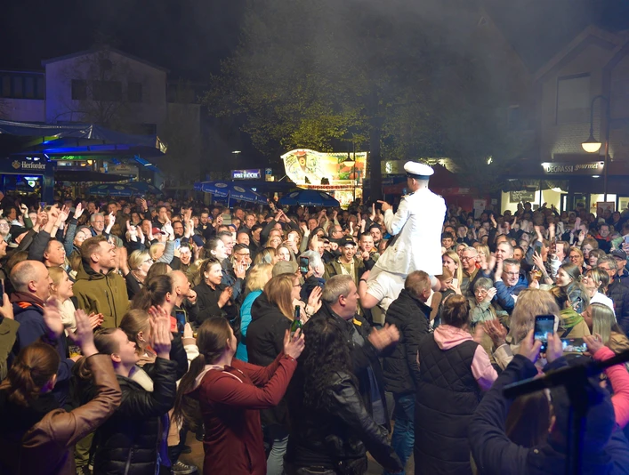 Große Menschenmenge bei Nacht, darunter ein Entertainer in weißer Kleidung auf einer erhöhten Bühne.