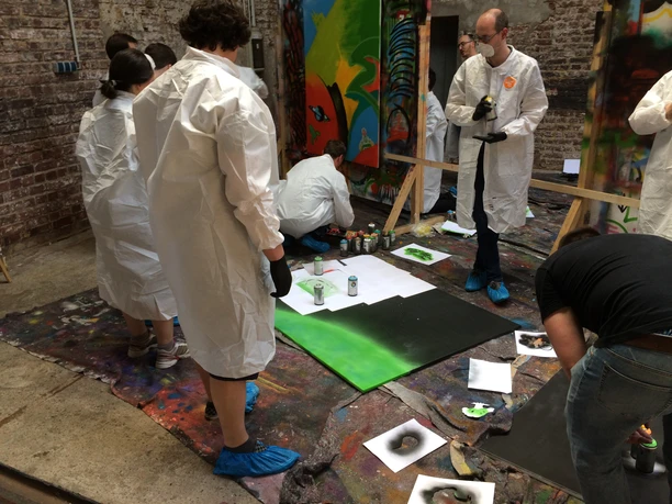 Cologne Graffiti. Arbeit an der Leinwand Personen in Schutzanzügen sprayen Graffiti in einem Kunst-Workshop in einem industriellen Raum.</p>