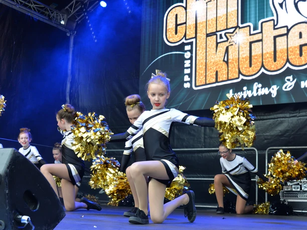 Eine Gruppe junger Cheerleader in schwarz-weißen Outfits performt vor einer großen Bühne.