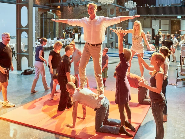 Westar. Zeigen was in uns steckt. Akrobatik Personen trainieren Akrobatik in einem lichtdurchfluteten Raum mit Ziegelwänden und großen Fenstern.