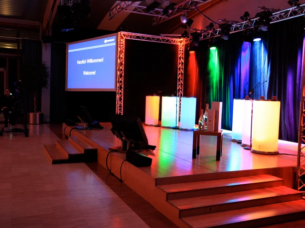 WeQuiz. Das Quizevent. Bühne Illuminated stage with multicolored spotlights, podium and "Welcome" projector screen.</p> <p