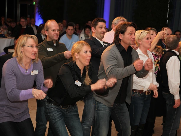 WeQuiz. Das Quizevent. Aktivrunde People in casual clothes dance synchronously in a group in an event room.</p> <p