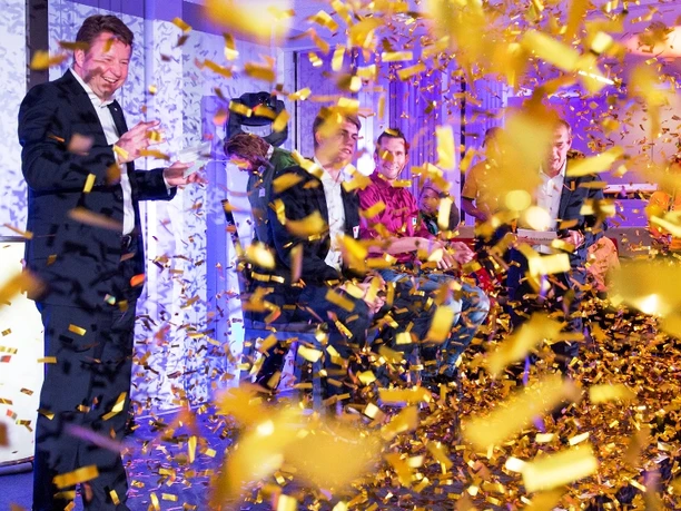 WeQuiz. Das Quizevent. Siegerehrung A man in a suit smiles as golden confetti falls at an event.